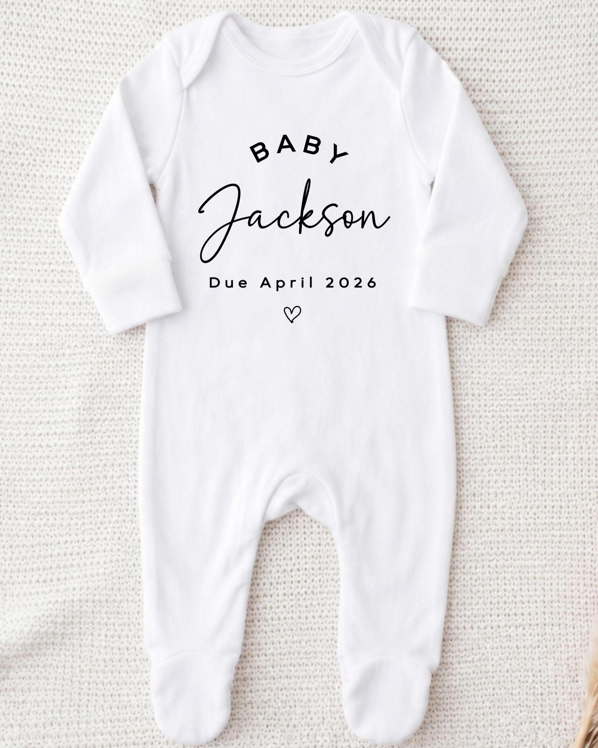 A white onesie with the text "BABY JACKSON Due April 2026" printed on it.