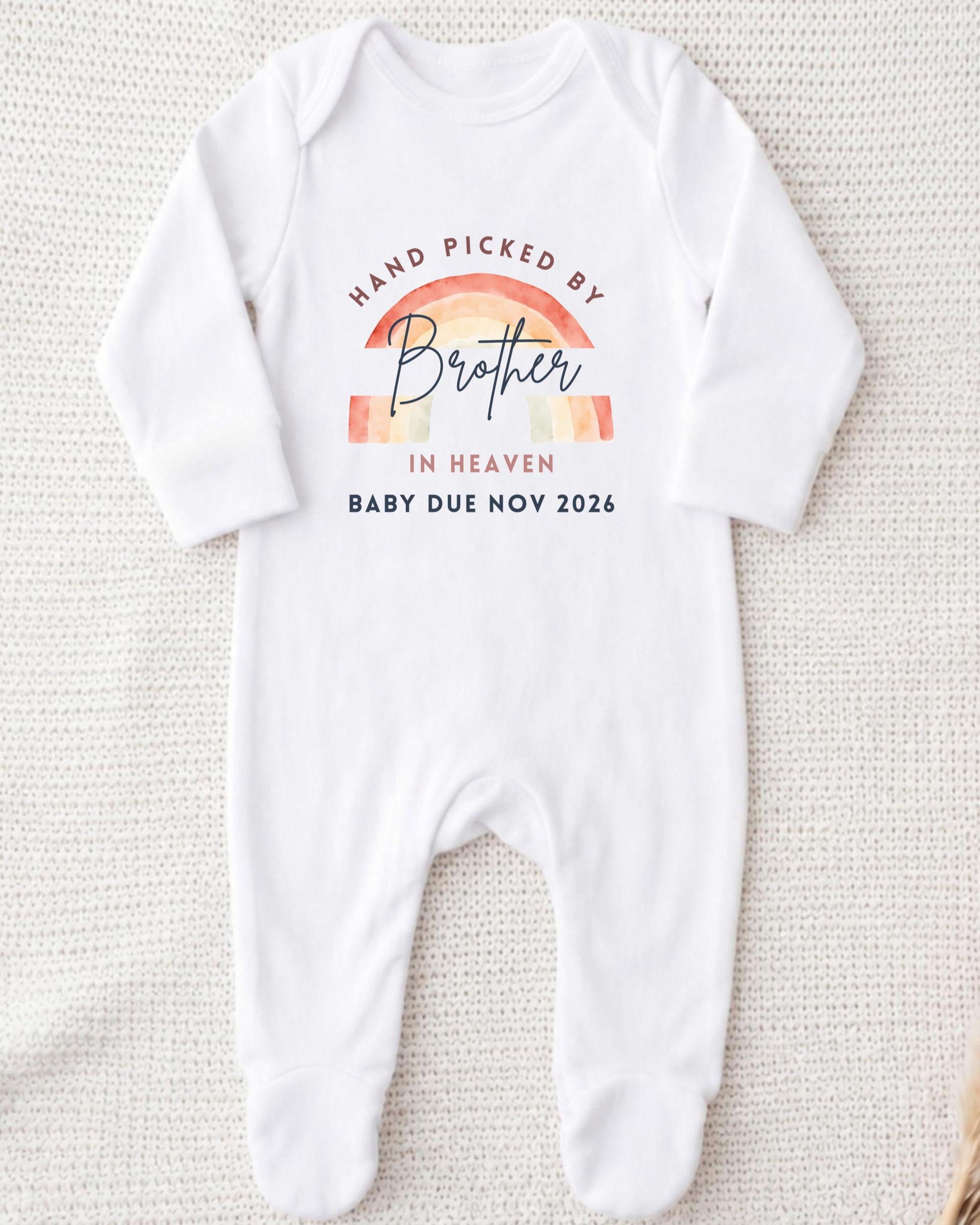A white onesie with a graphic design on it, which says "Hand picked by Brother in Heaven Baby due Nov 2026".