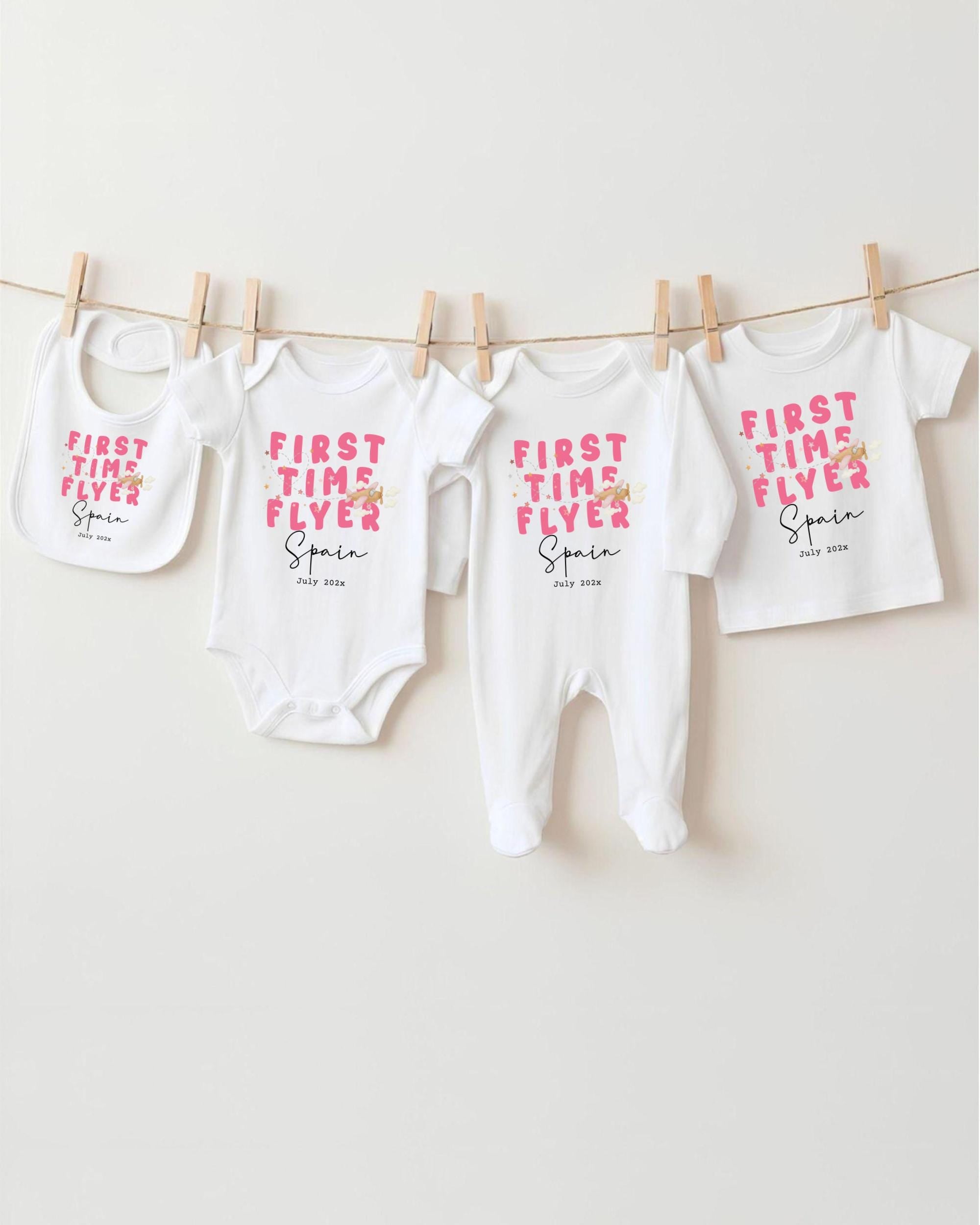 A row of four white baby clothes, including onesies and bibs, hanging on a clothesline.