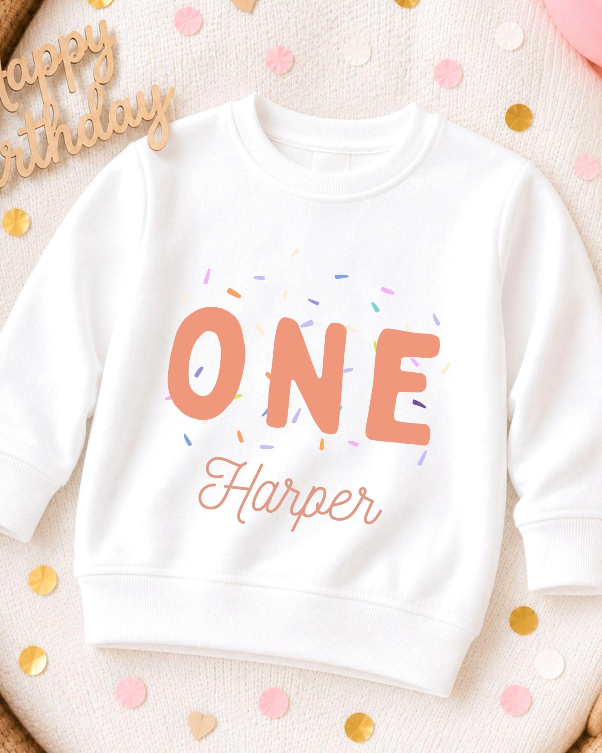 A white sweatshirt with the text "ONE Harper" printed on it, surrounded by colorful confetti.