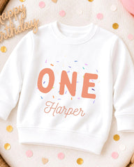 A white sweatshirt with the text "ONE Harper" printed on it, surrounded by colorful confetti.