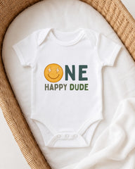 A white onesie with a smiley face and the text "ONE HAPPY Dude" printed on it, laid out on a white blanket.