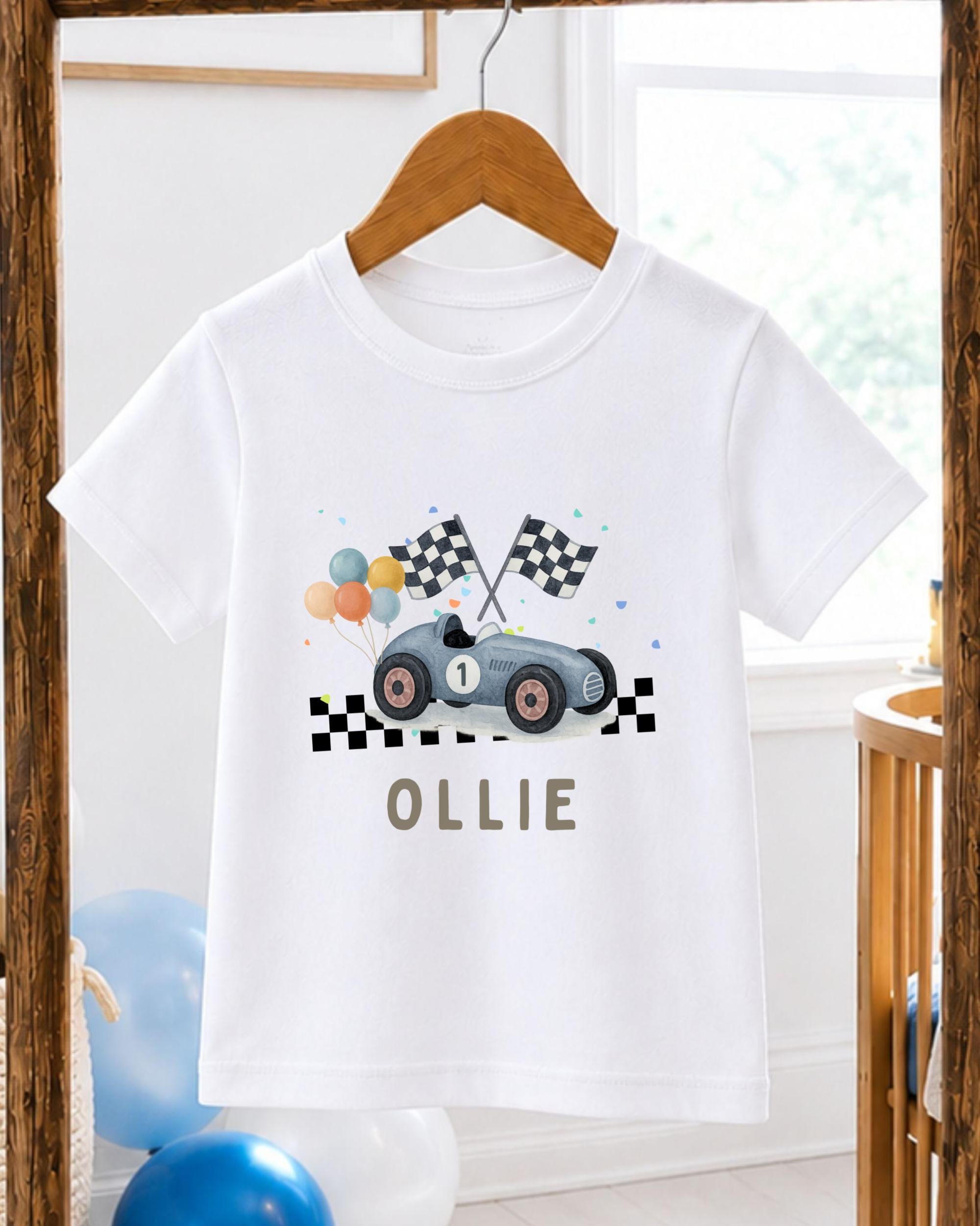 A white t-shirt with a graphic design of a race car and checkered flags, along with the name "Ollie" printed on it.