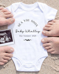A white onesie with the text "SEA YOU SOON Baby Whalley Due Summer 2026" printed on it, along with an image of an Ultrasound scan of a baby's belly.