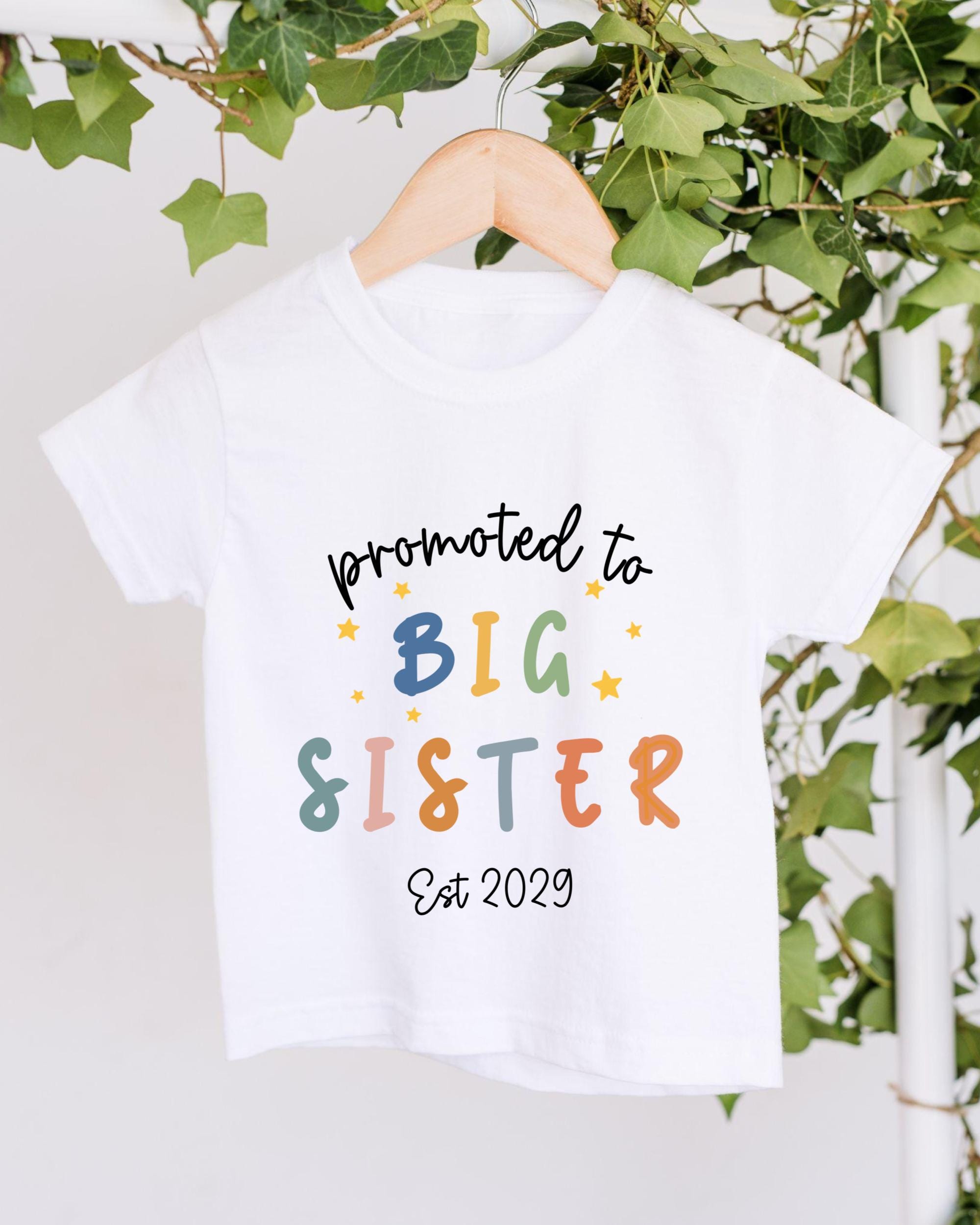 A white t-shirt with text that says "promoted to BIG SISTER Est 2029" printed on it.