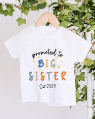 A white t-shirt with text that says "promoted to BIG SISTER Est 2029" printed on it.