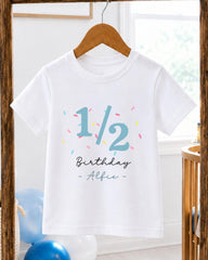A white t-shirt with a birthday message printed on it, hanging on a wooden hanger.