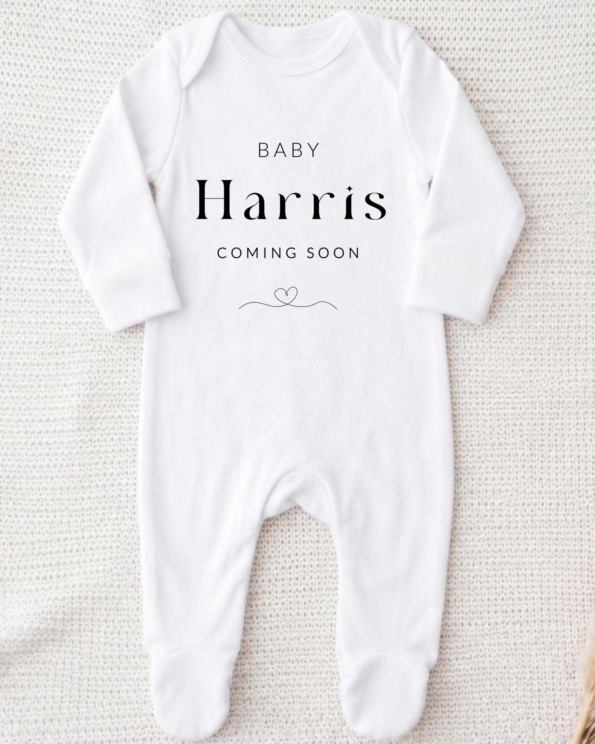 A white onesie with the text "BABY Harris COMING SOON" printed on it.