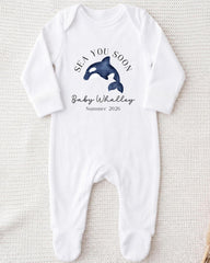 A white onesie with a graphic of a baby whale and text that says "SEA YOU SOON Baby Whalley Summer 2026".