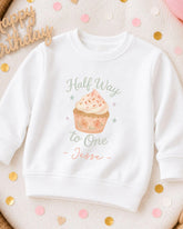 A white sweatshirt with a graphic of a cupcake and the text "Half Way to One Jesse" printed on it, surrounded by confetti.