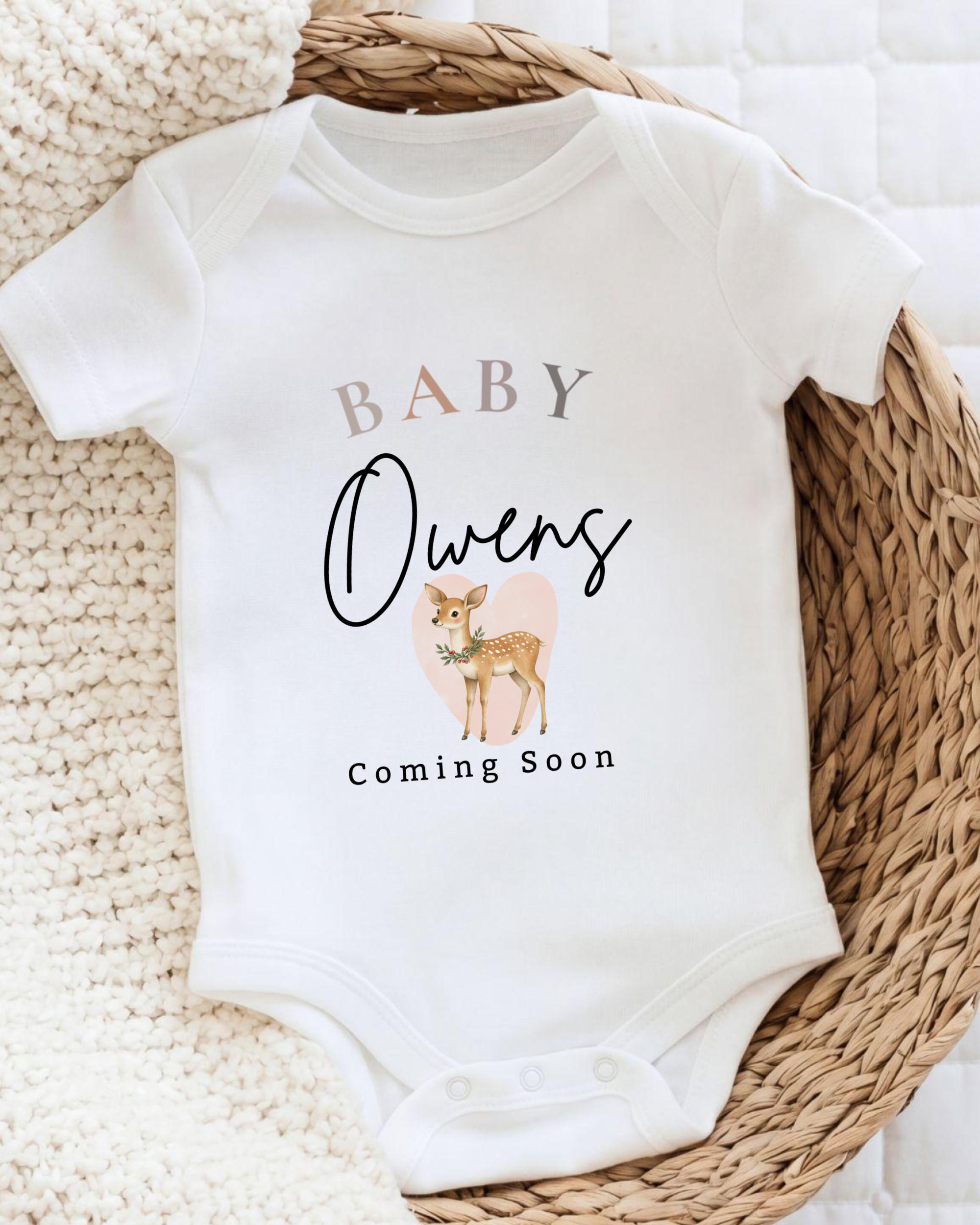 A white baby onesie with the text "BABY Owens Coming Soon" printed on it, along with an illustration of a deer.
