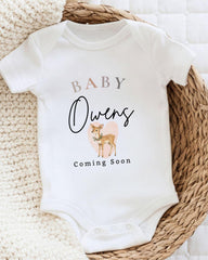 A white baby onesie with the text "BABY Owens Coming Soon" printed on it, along with an illustration of a deer.