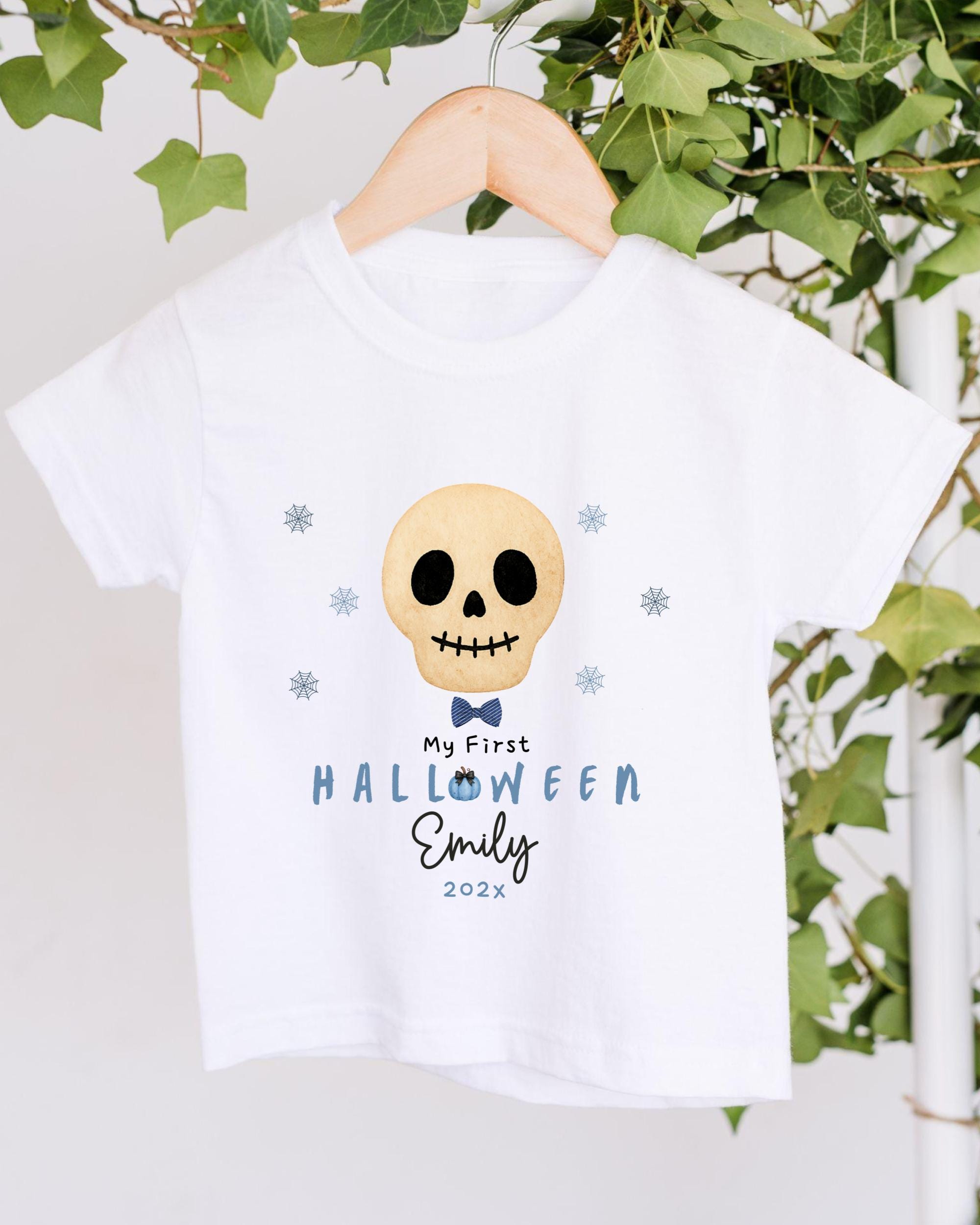 A white t-shirt with a skull design and text printed on it, hanging on a wooden hanger.