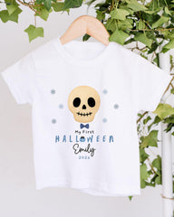 A white t-shirt with a skull design and text printed on it, hanging on a wooden hanger.
