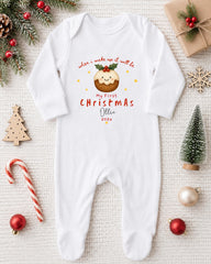 A white onesie with a Christmas-themed design, featuring a smiling puddigot, is displayed on a white background alongside various Christmas decorations and gifts.