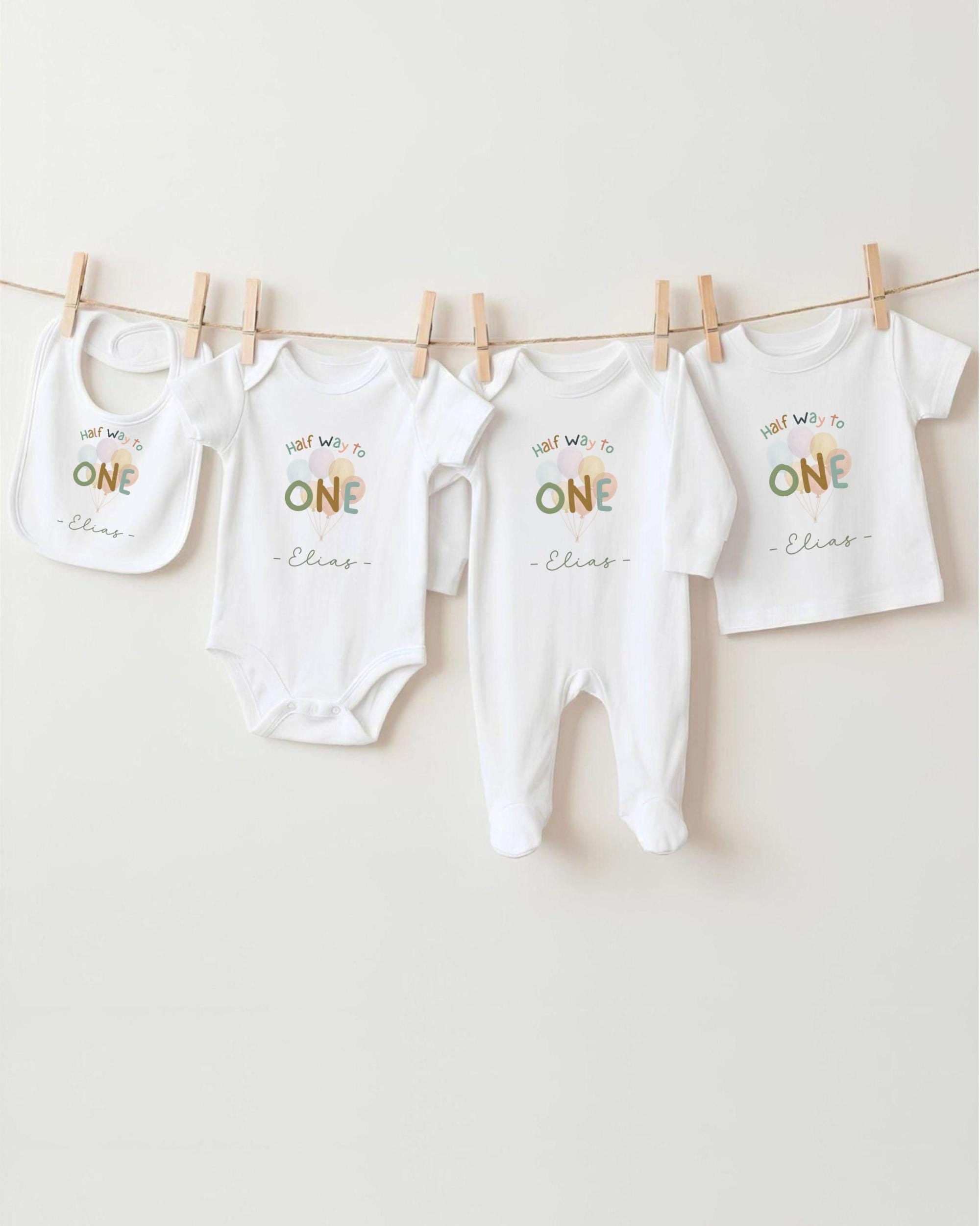 A row of four white baby clothes, including bibs and onesies, hanging on a clothesline.