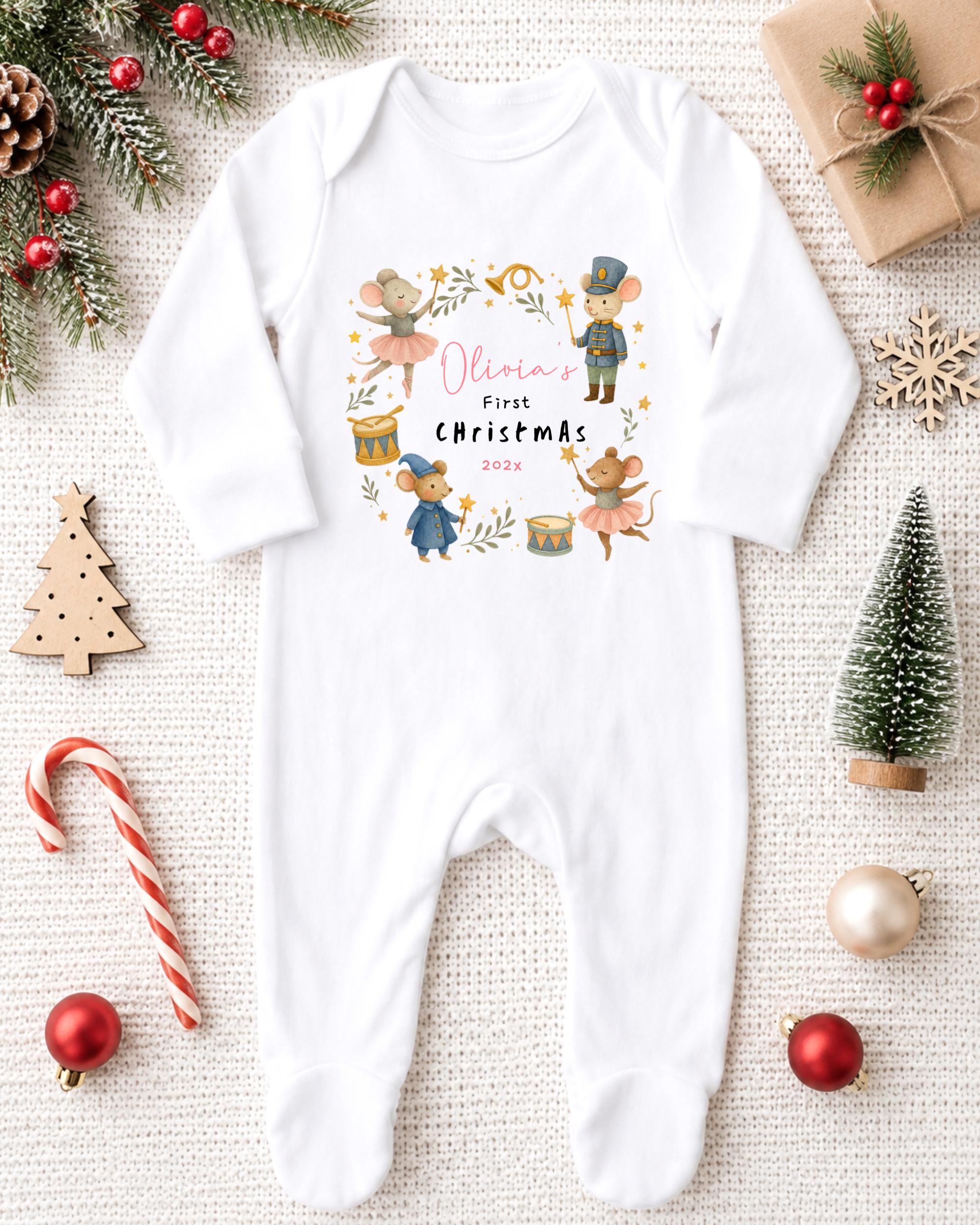 A white onesie with a Christmas-themed design, featuring illustrations of mice and other holiday-themed characters, is displayed on a white background alongside various Christmas decorations.