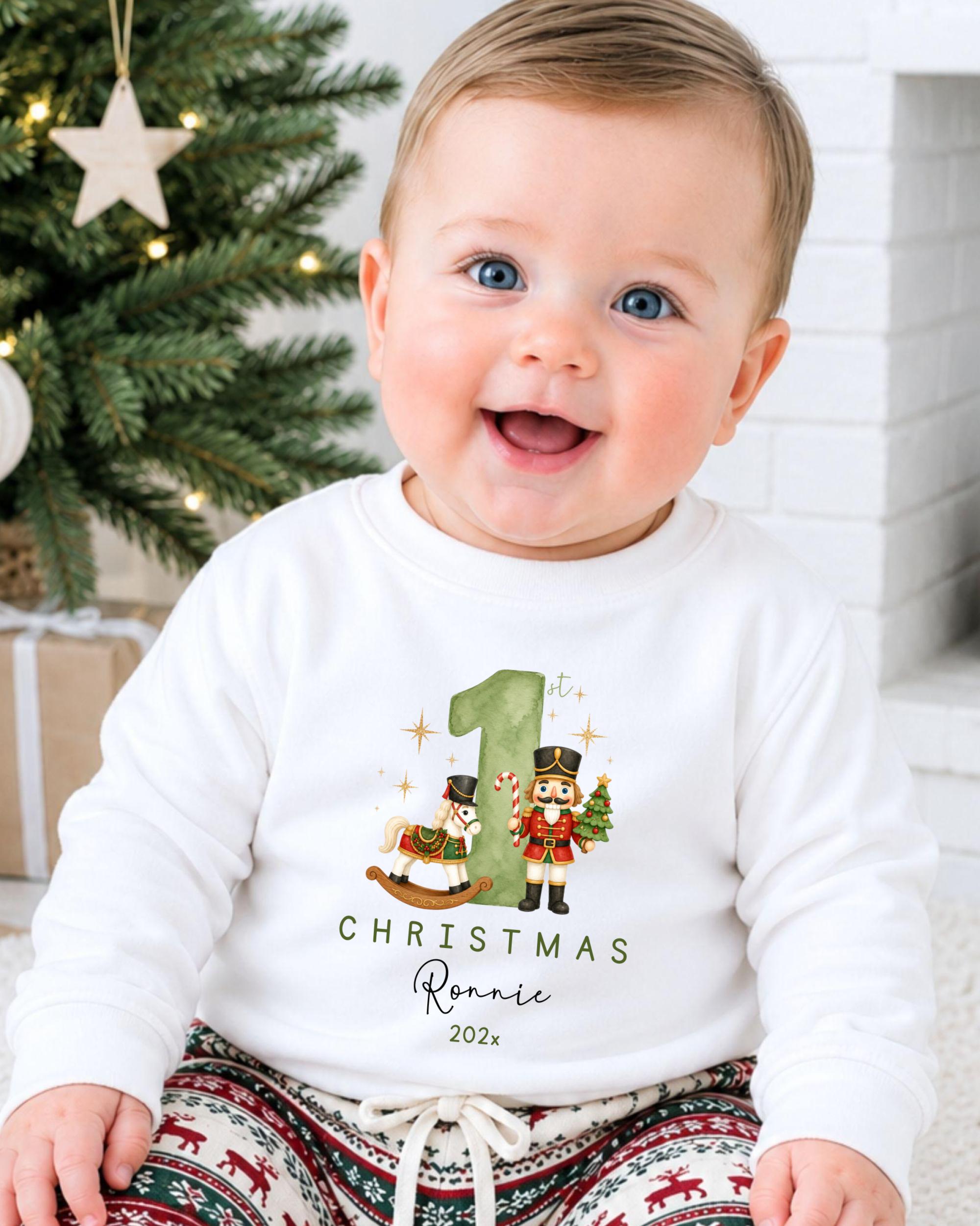 A smiling baby boy wearing a white shirt with a Christmas-themed design and text.