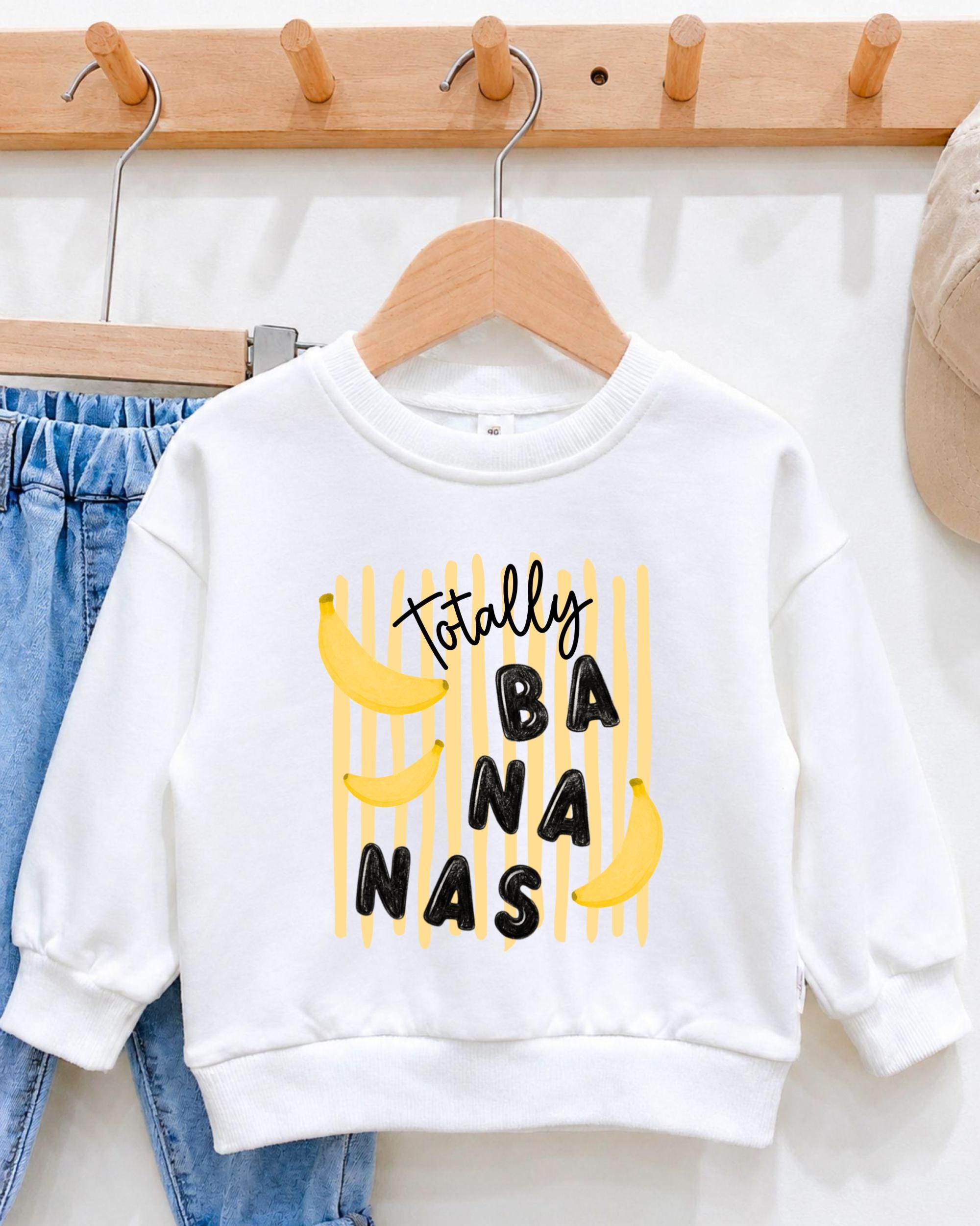 A white sweatshirt with a playful graphic design featuring bananas and the text "Totally BANANA" printed on it.