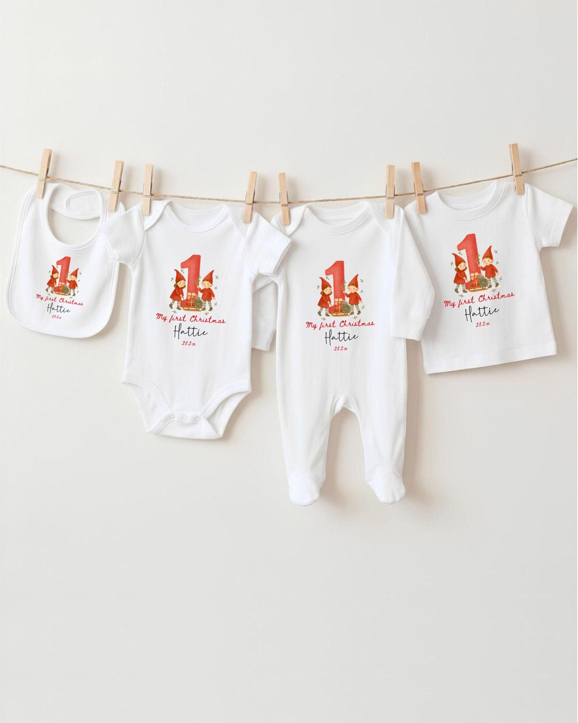 A row of white baby clothes with red and green Christmas-themed designs hanging on a clothesline.