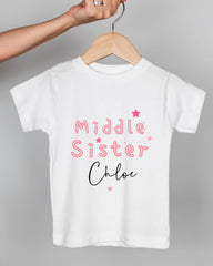 A white t-shirt with pink text and stars printed on it, being held by a person's hand.