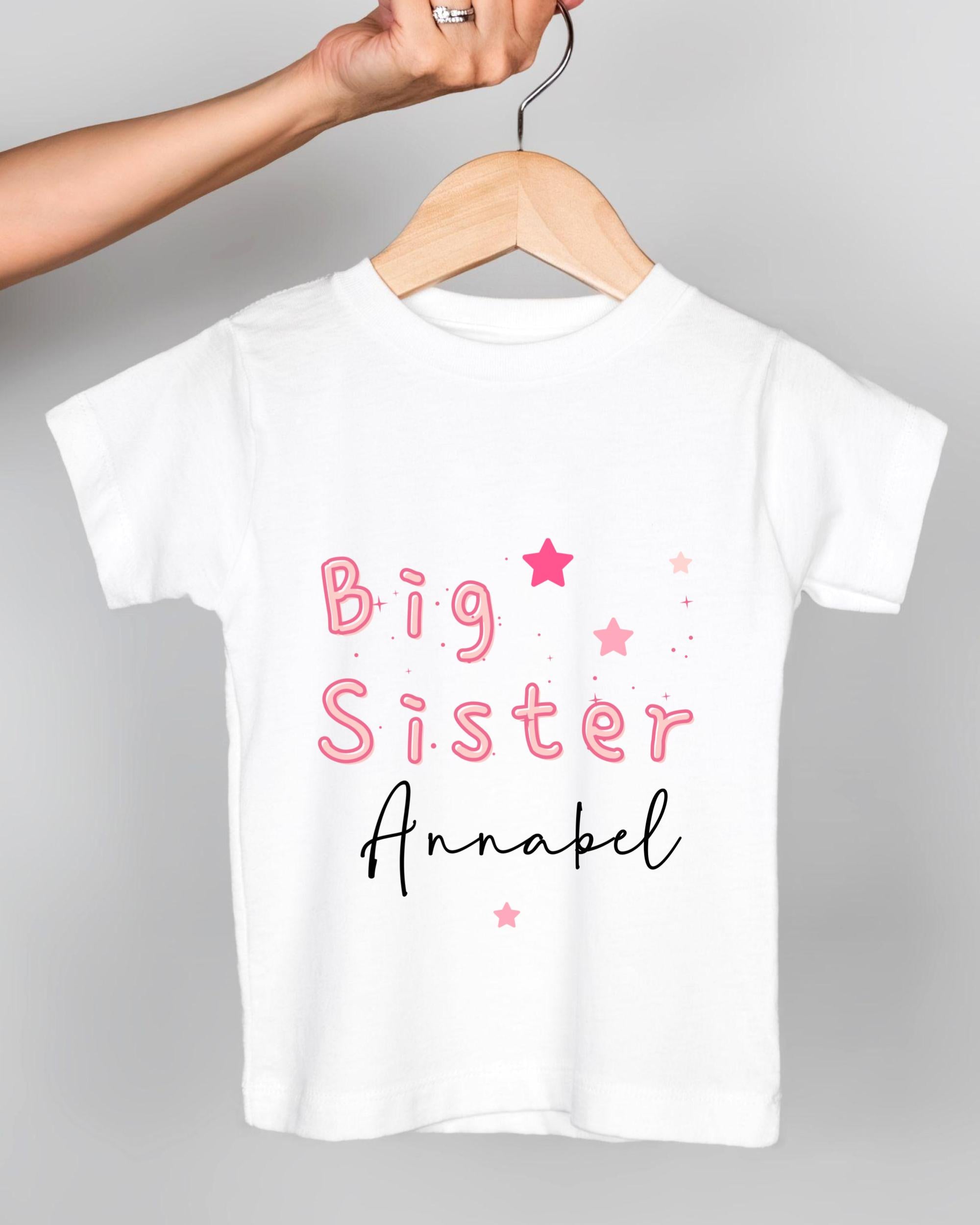 A white t-shirt with pink text and stars printed on it, being held by a person's hand.