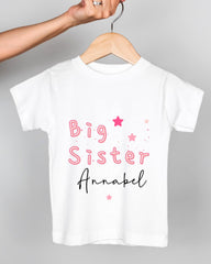 A white t-shirt with pink text and stars printed on it, being held by a person's hand.