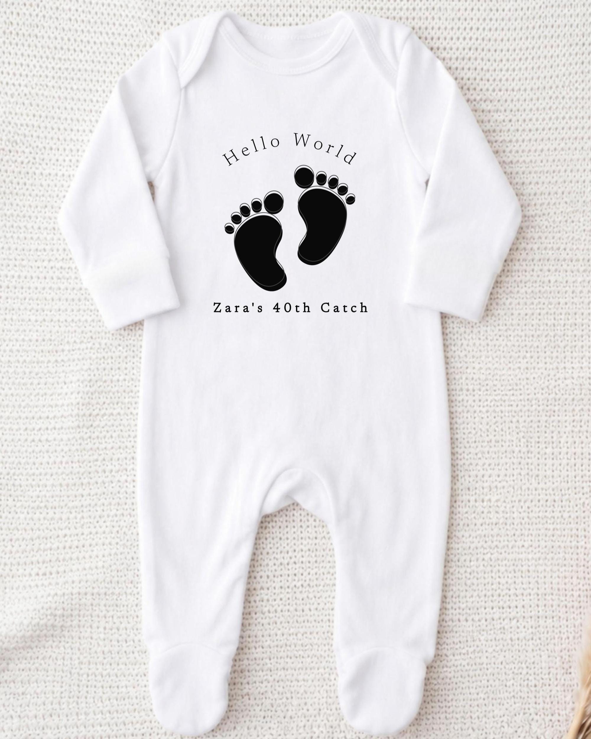 A white onesie with a black footprint design and text printed on it.