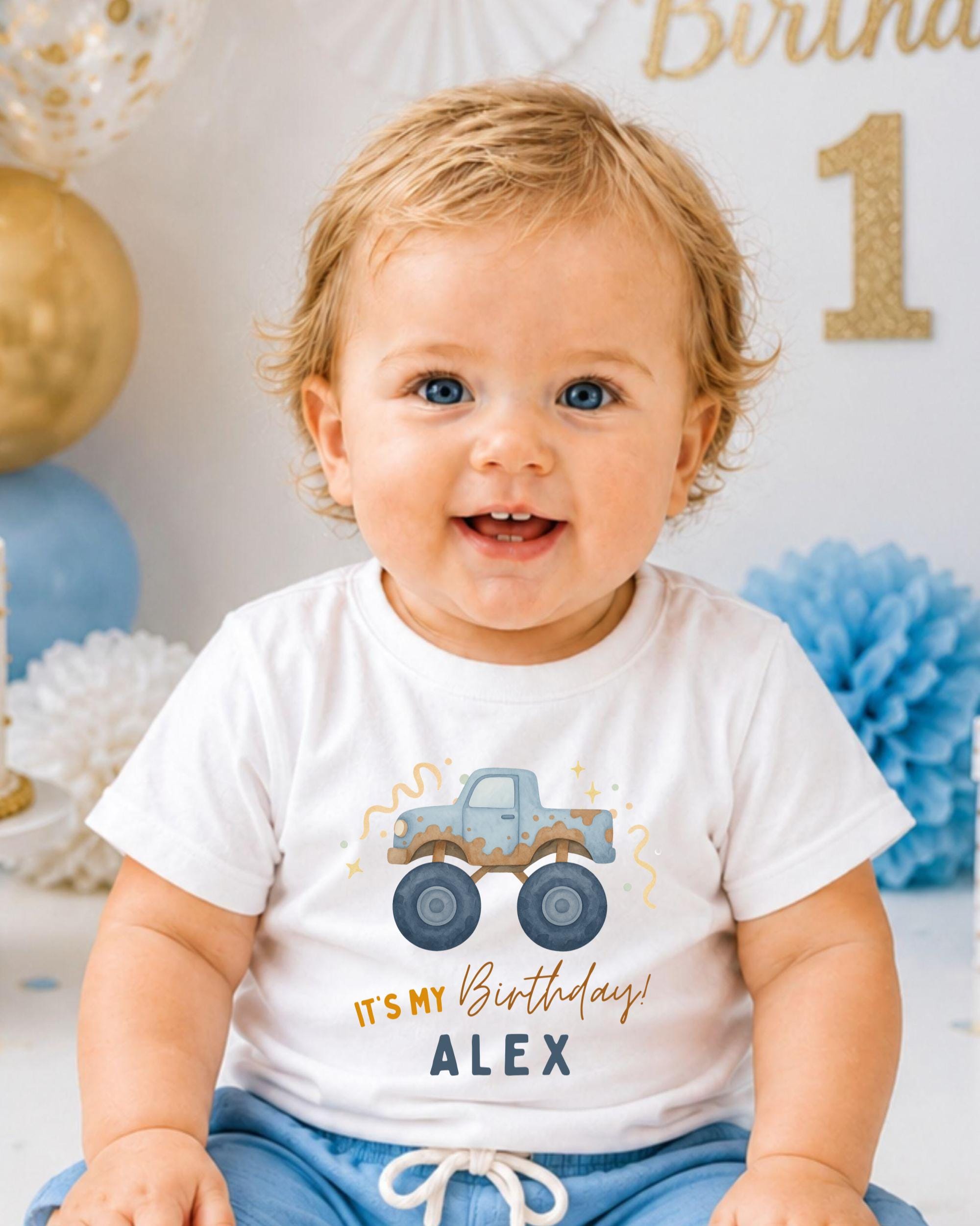 A smiling baby boy wearing a white t-shirt with a truck graphic and the text "It's my birthday Alex" printed on it.