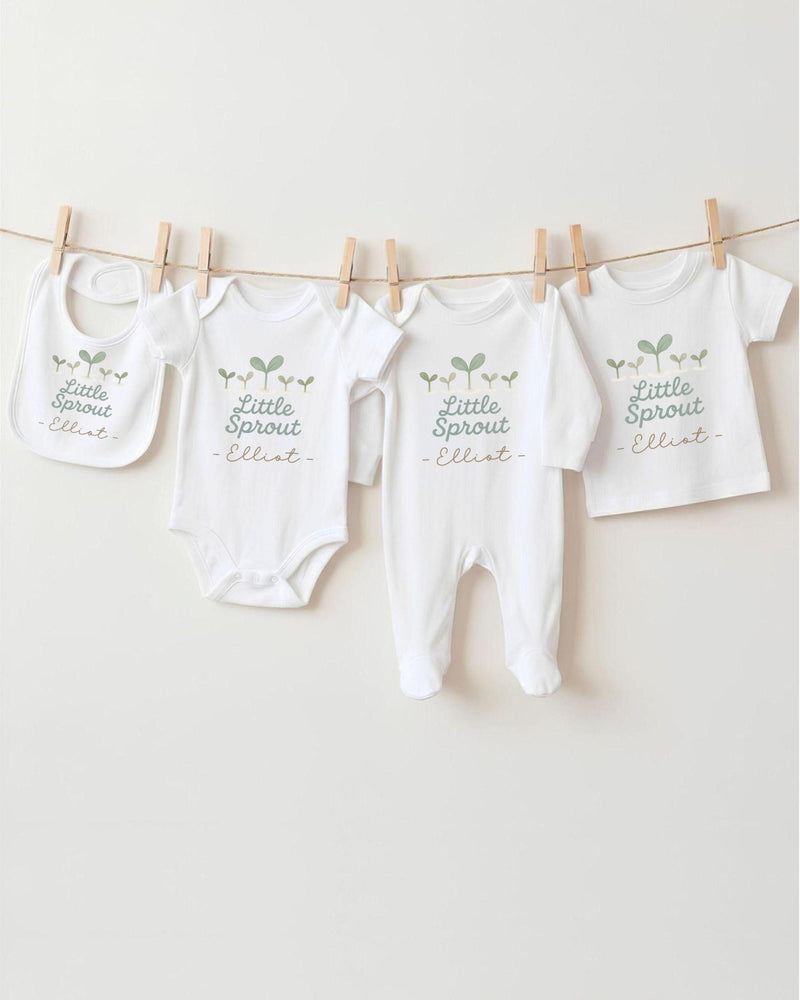 A row of four white baby clothes with the text "Little Sprout" printed on them, hanging on a clothesline.