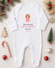 A white onesie with a fairy image and text, surrounded by Christmas decorations and ornaments.