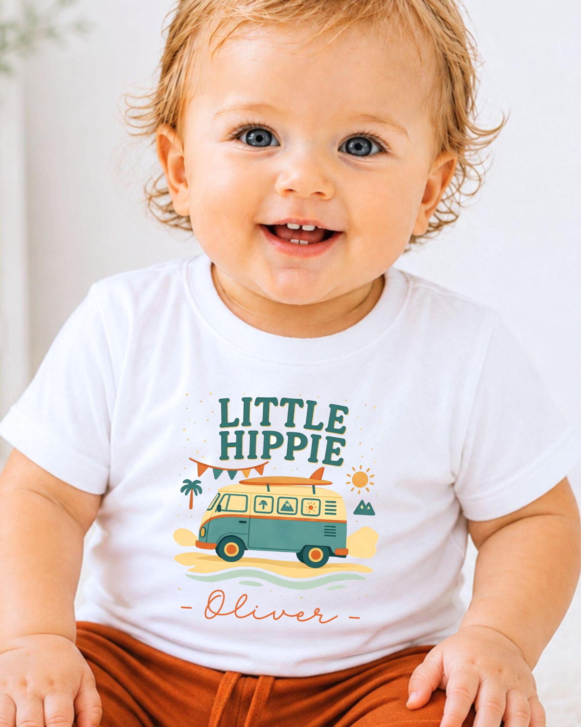 A smiling baby boy wearing a white t-shirt with a colorful graphic design and text.