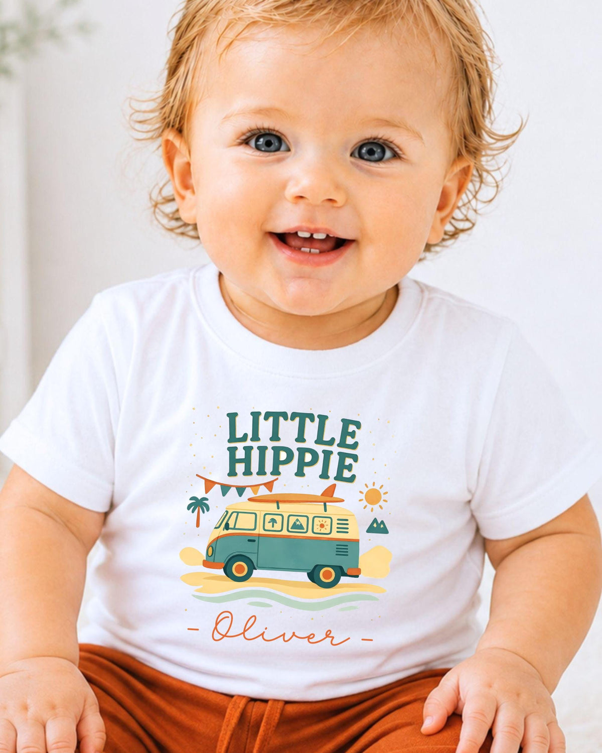 A smiling baby boy wearing a white t-shirt with a colorful graphic design and text.