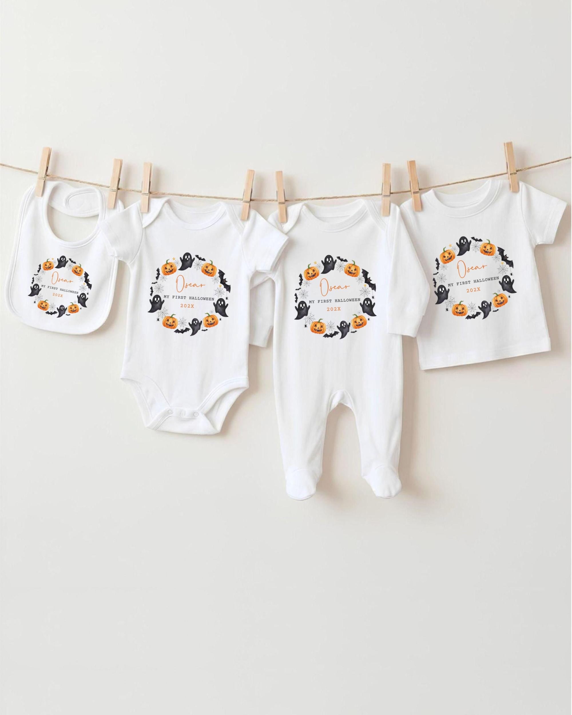 A row of four white baby clothes with Halloween-themed designs hanging on a clothesline.