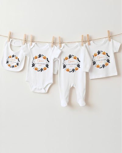 A row of four white baby clothes with Halloween-themed designs hanging on a clothesline.