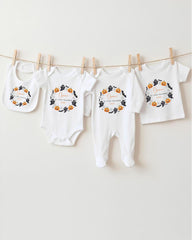 A row of four white baby clothes with Halloween-themed designs hanging on a clothesline.