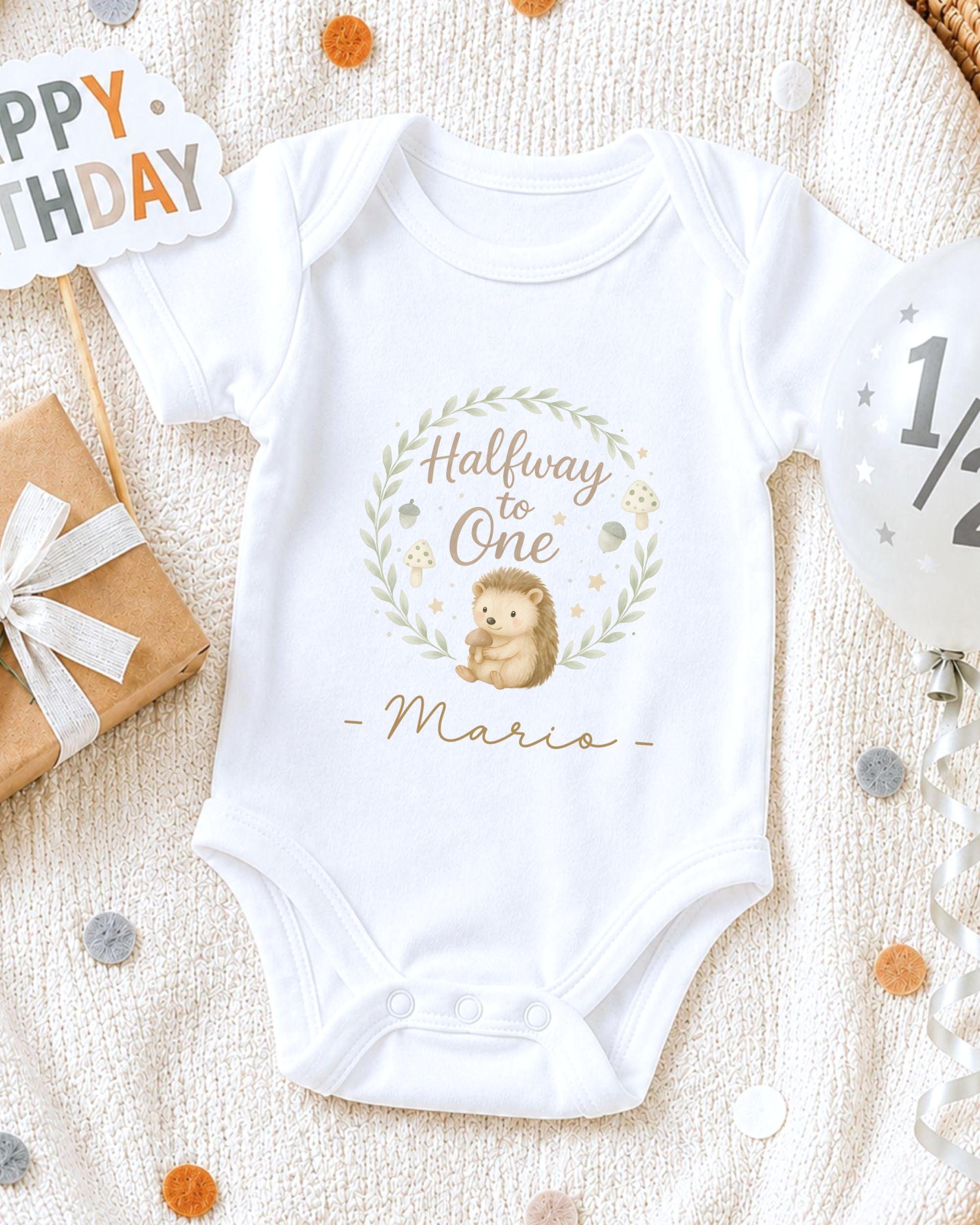 A white onesie with a hedgehog design and the text "Halfway to One Mario" printed on it, along with a "Happy Birthday" sign and confetti.