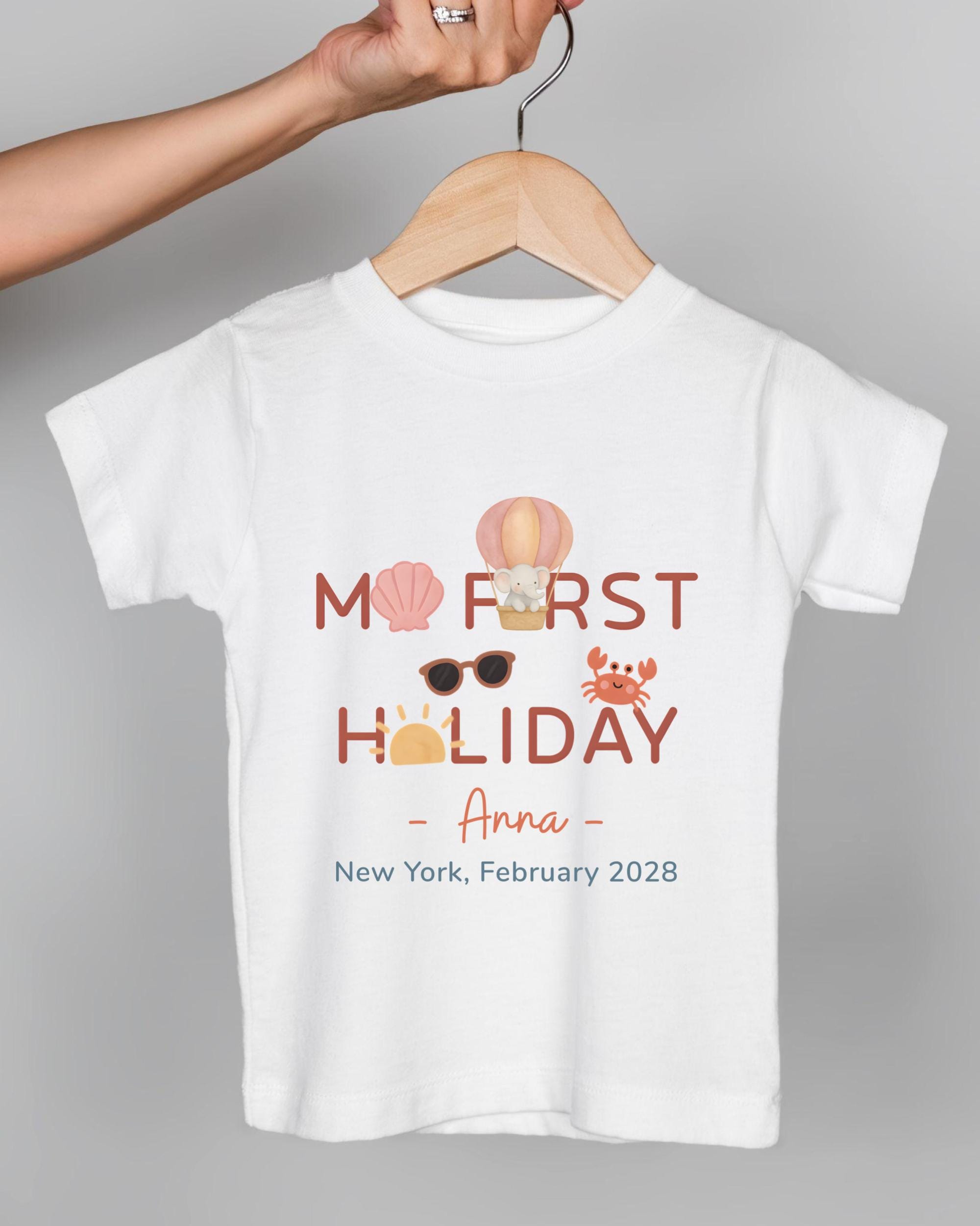A white t-shirt with a graphic design featuring a hand holding a hanger with a t-shirt, a crab, sunglasses, and a beach scene.
