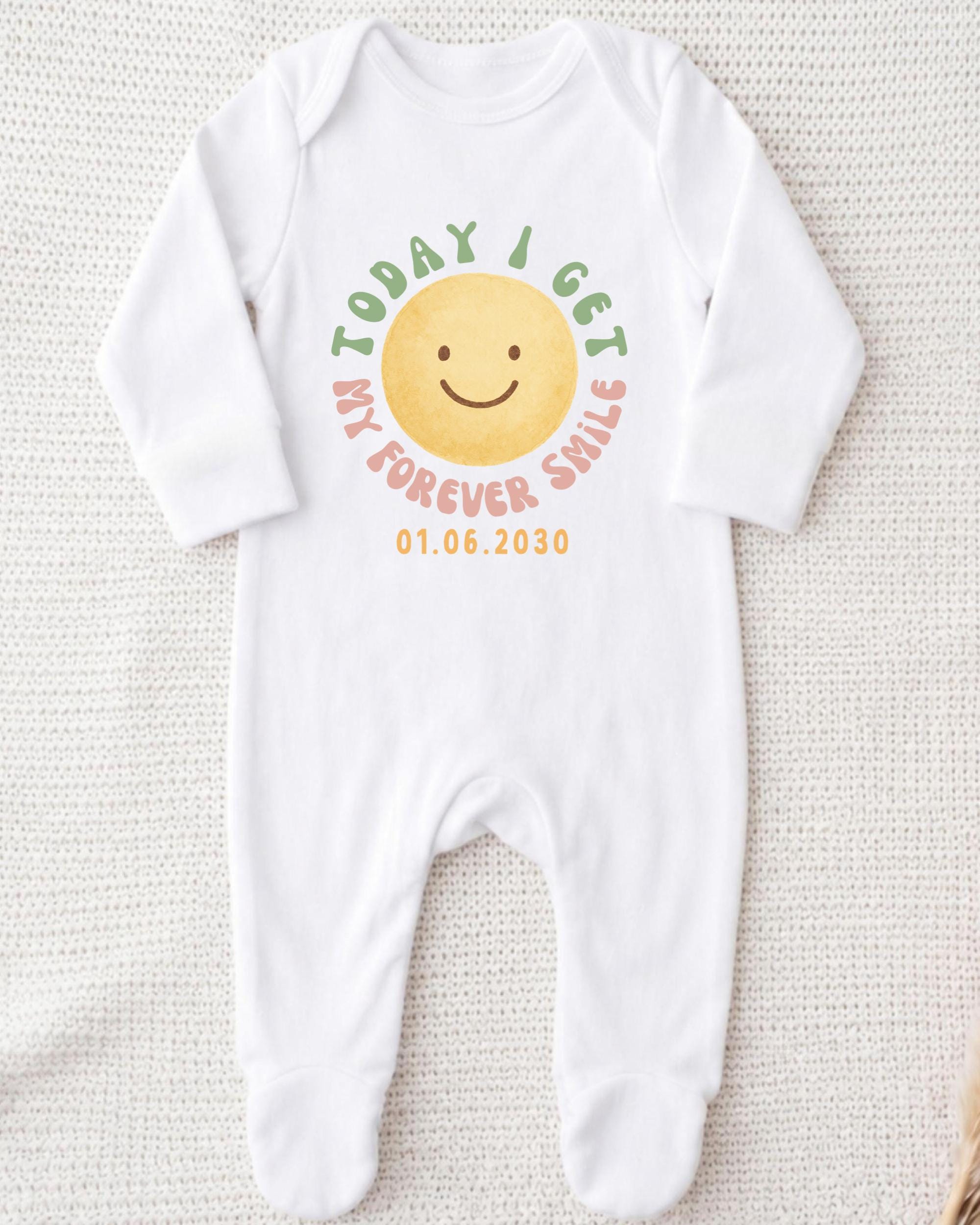 A white onesie with a smiley face design and text printed on it.
