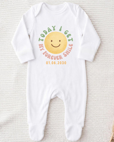 A white bodysuit with a smiley face design and text printed on it.