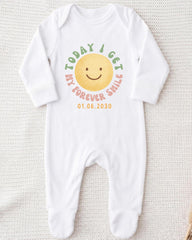 A white onesie with a smiley face design and text printed on it.