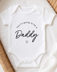 A white baby onesie with the text "You're going to be a Daddy" printed on it.