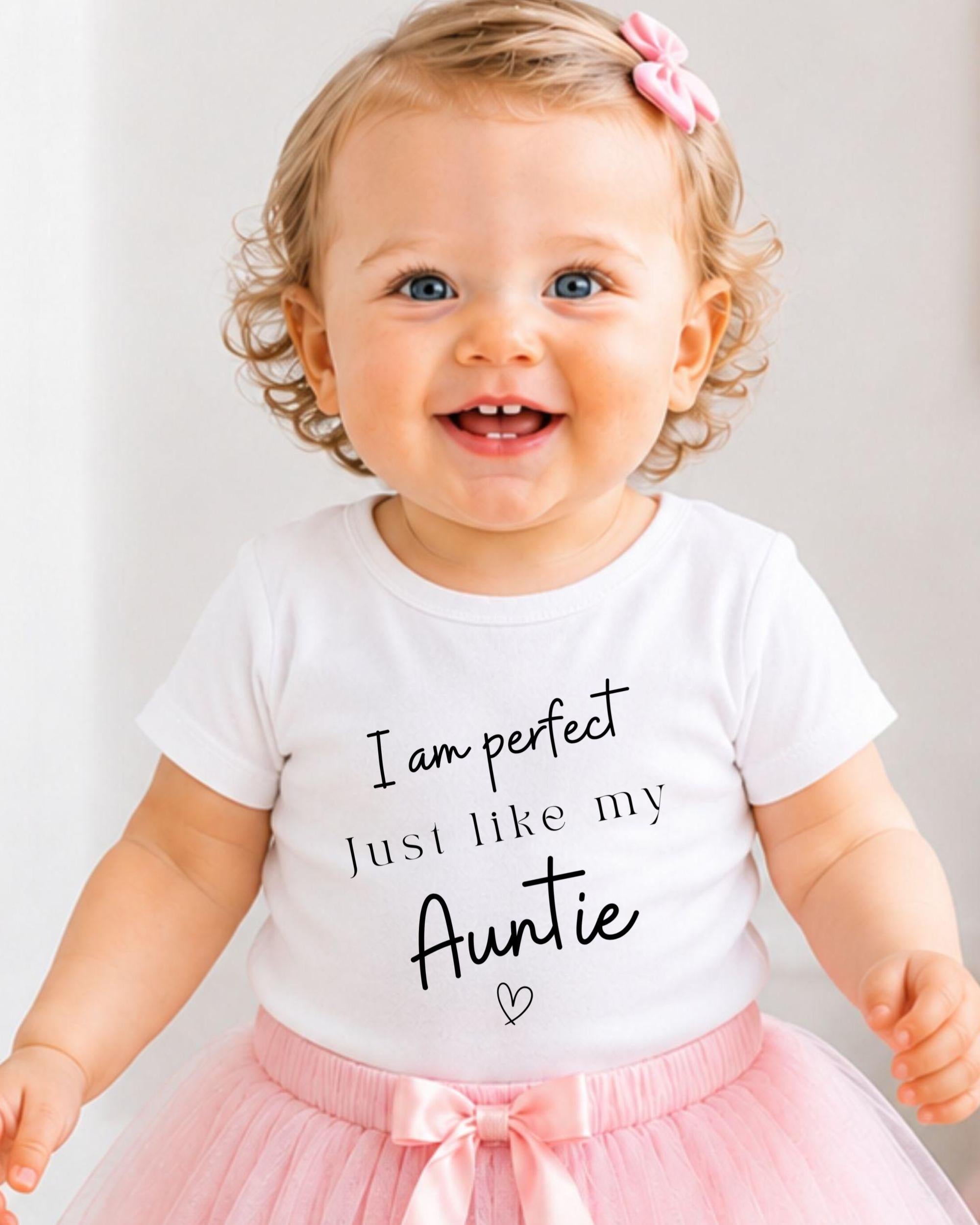 A smiling baby girl wearing a white t-shirt with text and a pink bow in her hair.