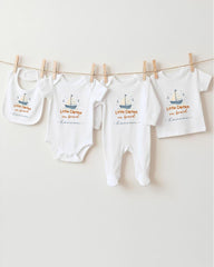 A row of four white baby clothes with the text "Little Captain on board" printed on them, hanging on a clothesline.