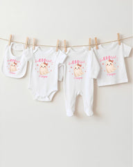 A collection of baby clothes, including onesies and bibs, hanging on a clothesline.