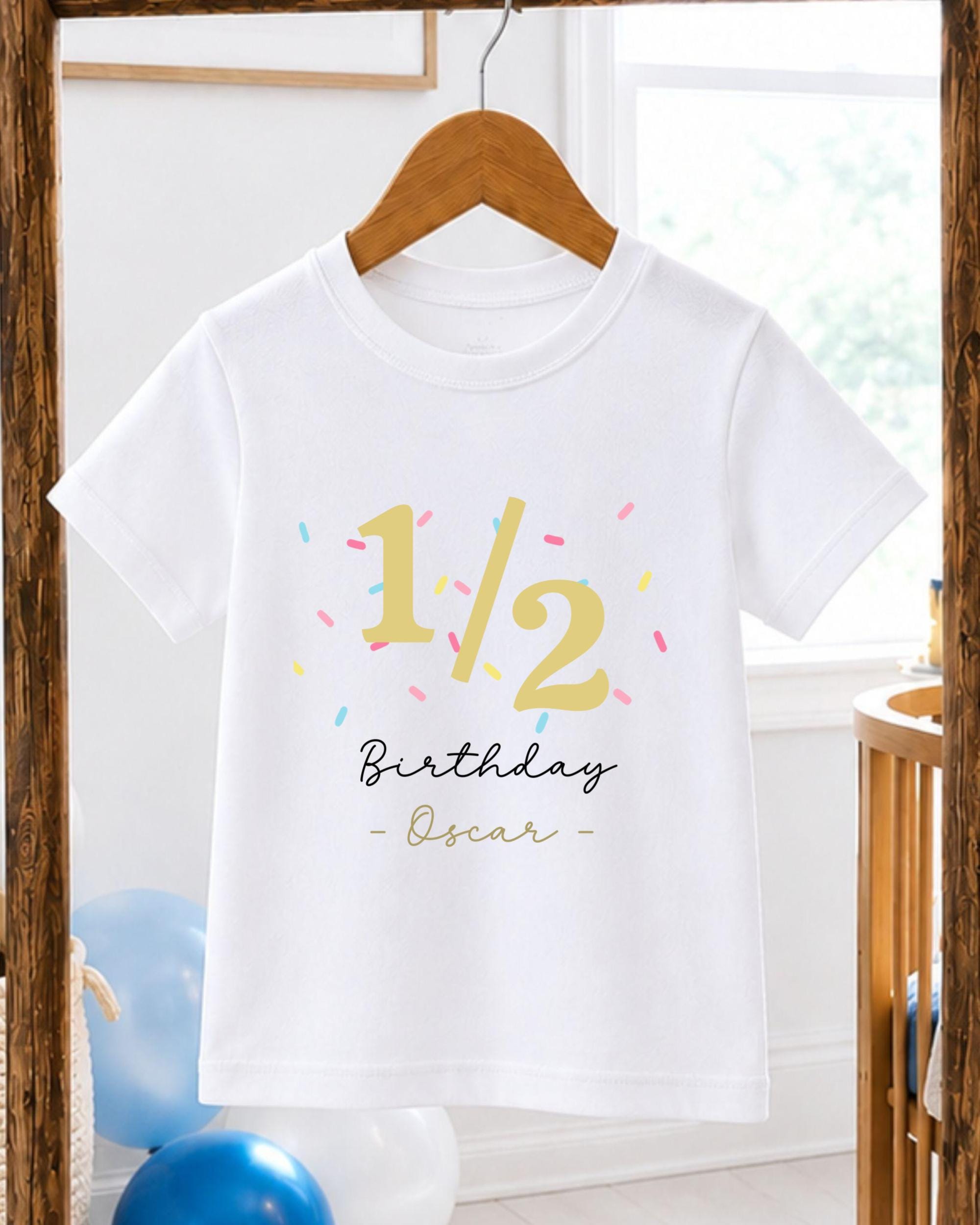 A white t-shirt with a birthday message printed on it, hanging on a wooden hanger.