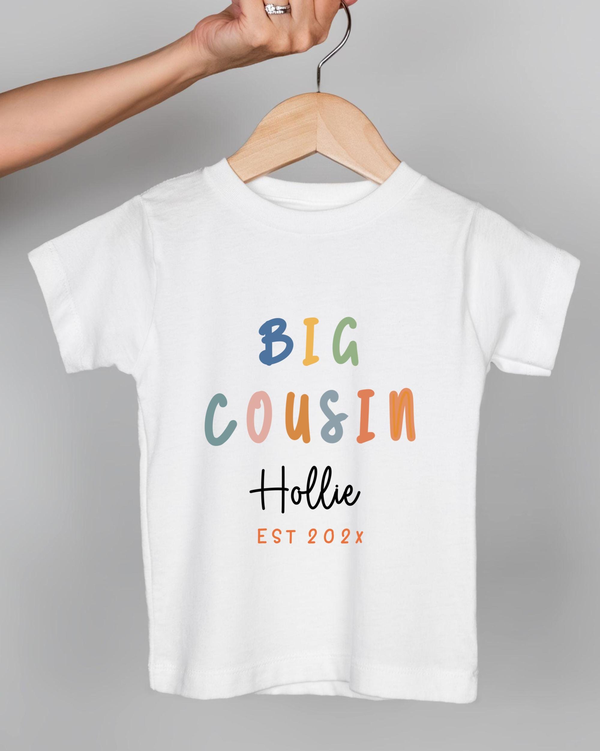 A person's hand is holding a white t-shirt with colorful text and graphics printed on it.