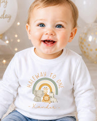 A smiling baby wearing a white shirt with a graphic of animals and the text "Halfway to one" printed on it.