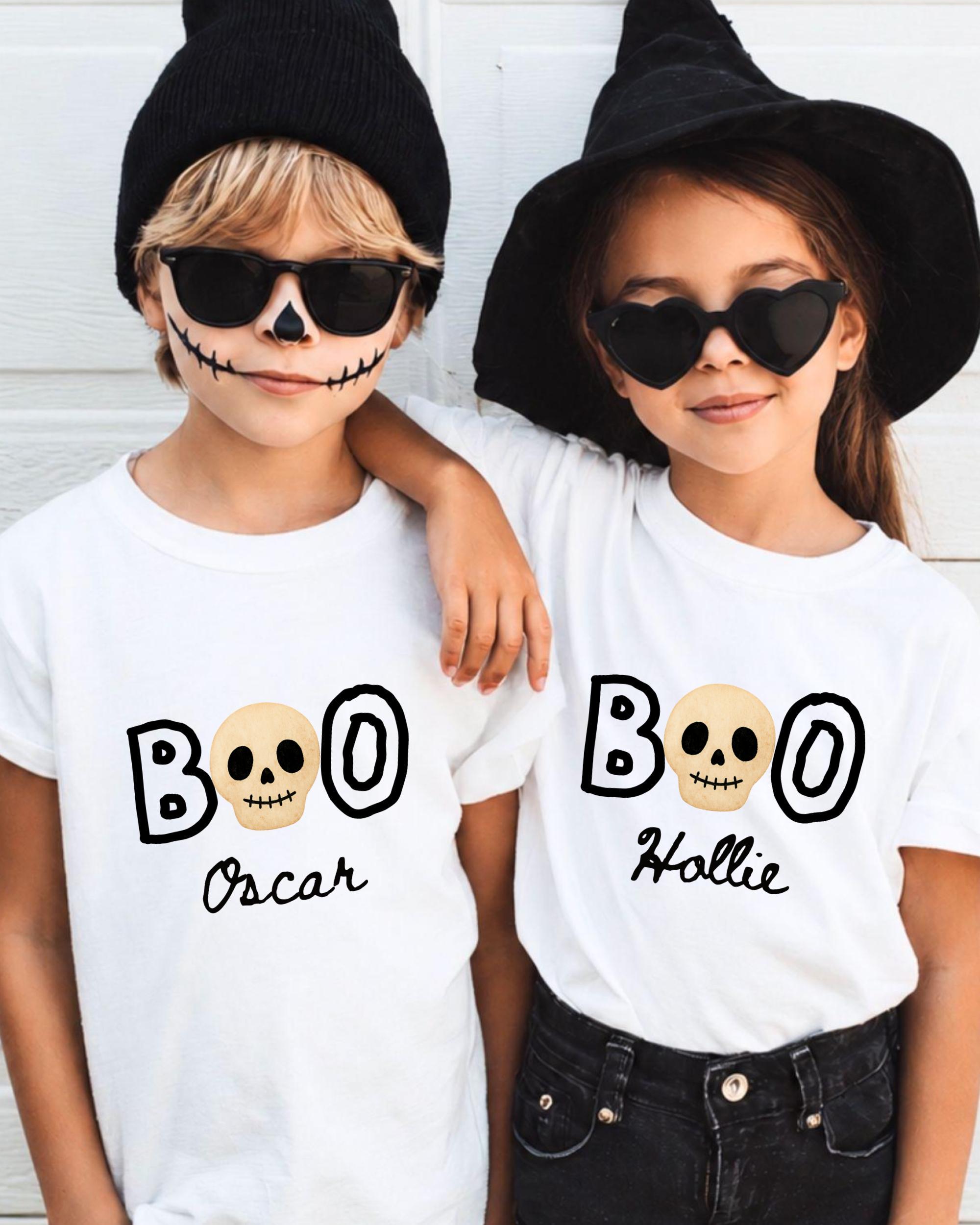 Two children wearing white t-shirts with the text "BOO" and "Hollie" printed on them, along with skull designs and a witch hat.