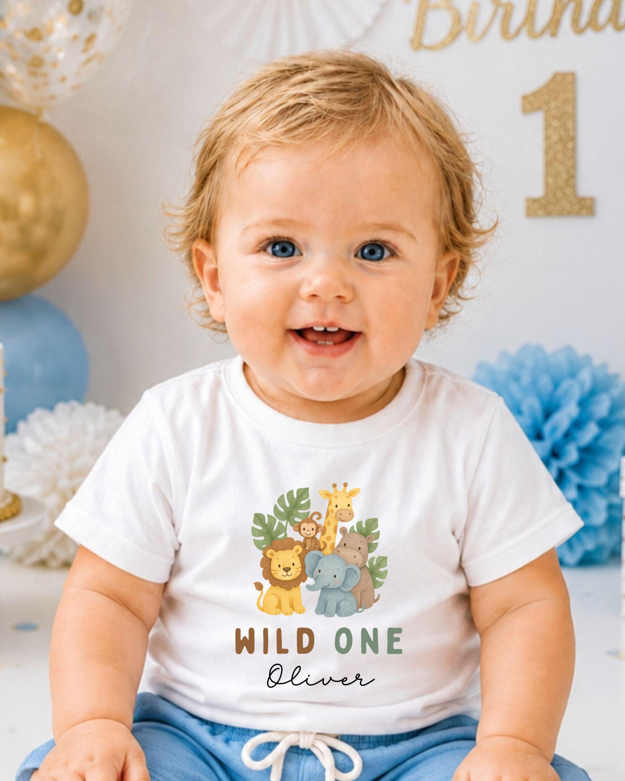 A smiling baby boy wearing a white t-shirt with a jungle animal design and the text "Wild One Oliver" printed on it.